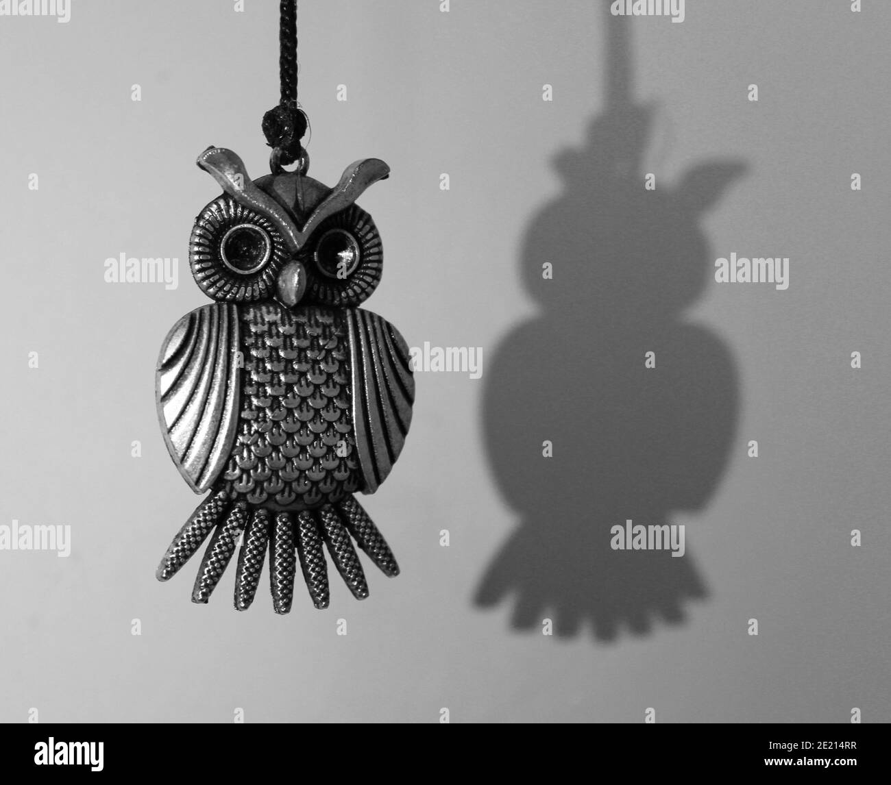 Ripresa in bianco e nero di una piccola lampada a sospensione metallica vicino al muro con la sua ombra Foto Stock