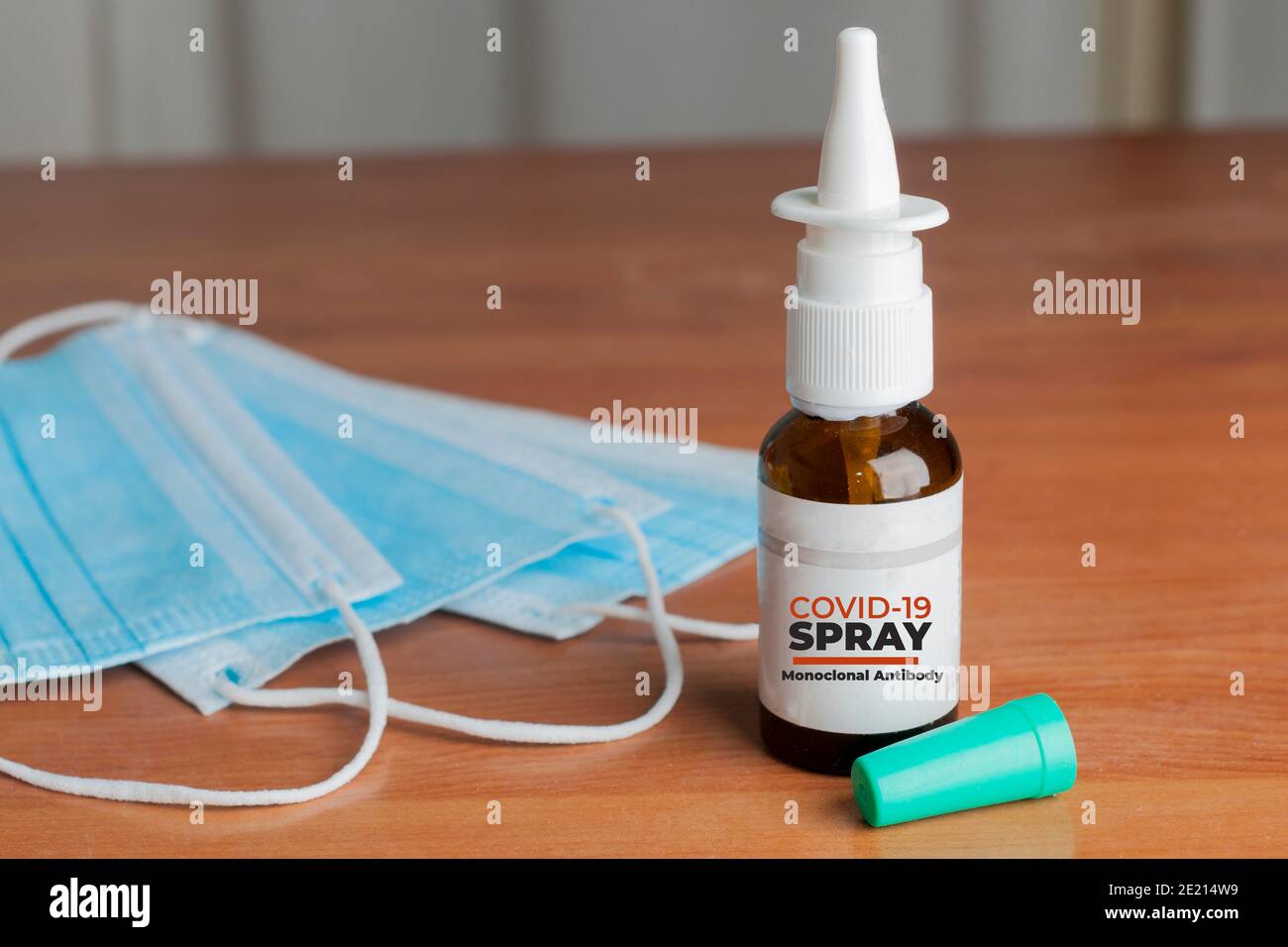Flacone di spray nasale anti covid-19 realizzato con anticorpi monoclonali su un tavolo di legno accanto ad alcune maschere chirurgiche Foto Stock