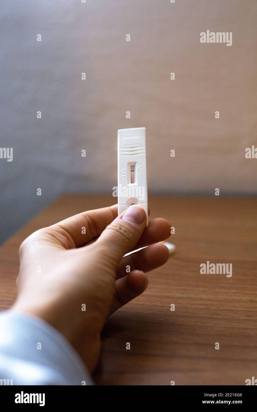 Tenendo la mano e mostrando un test negativo sugli anticorpi del sangue del coronavirus su un tavolo con parete bianca come sfondo Foto Stock