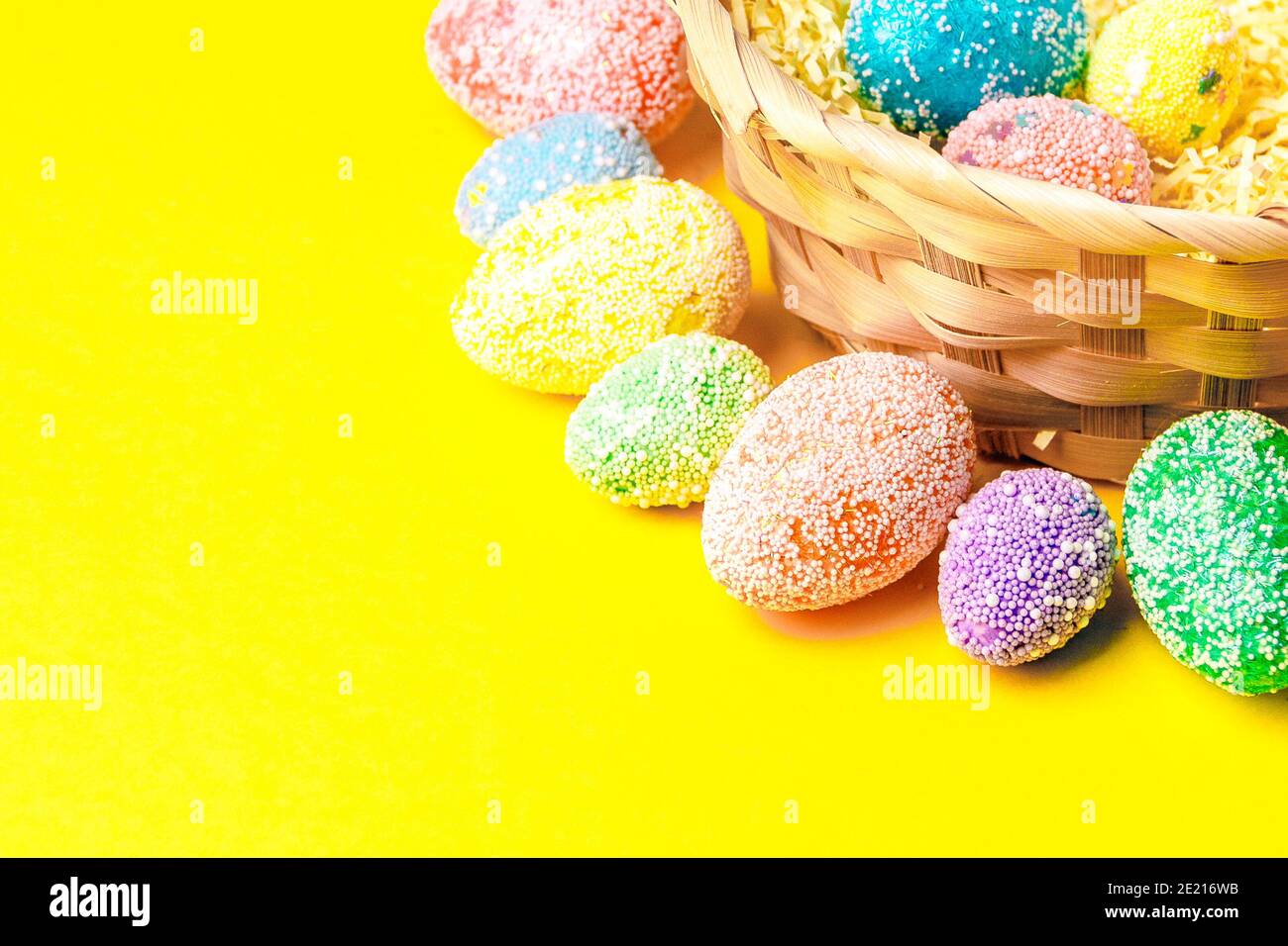 Buona Pasqua. Uova pastello in cestino su sfondo giallo piatto con spazio per il testo. Foto Stock