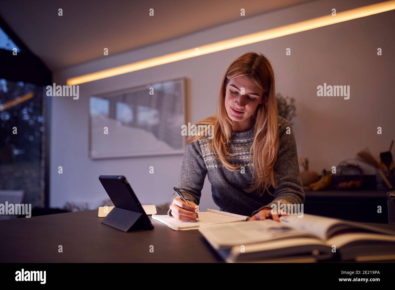 Evening Shot di Donna in cucina che lavora o studia da Casa con Digital Tablet Foto Stock