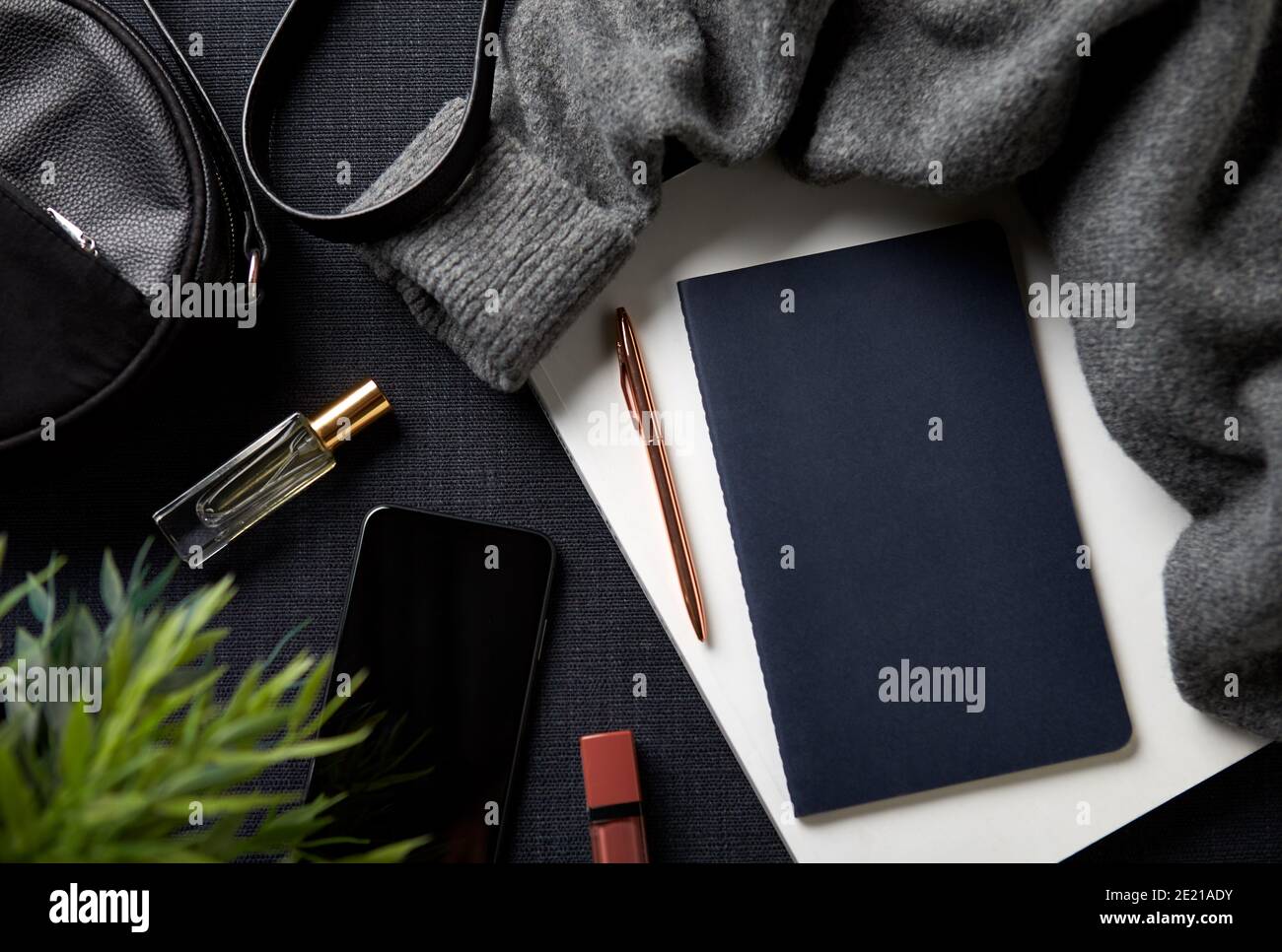 Flat Lay Lifestyle Shot con jumper Cosmetics notebook e borsa Su sfondo nero Foto Stock