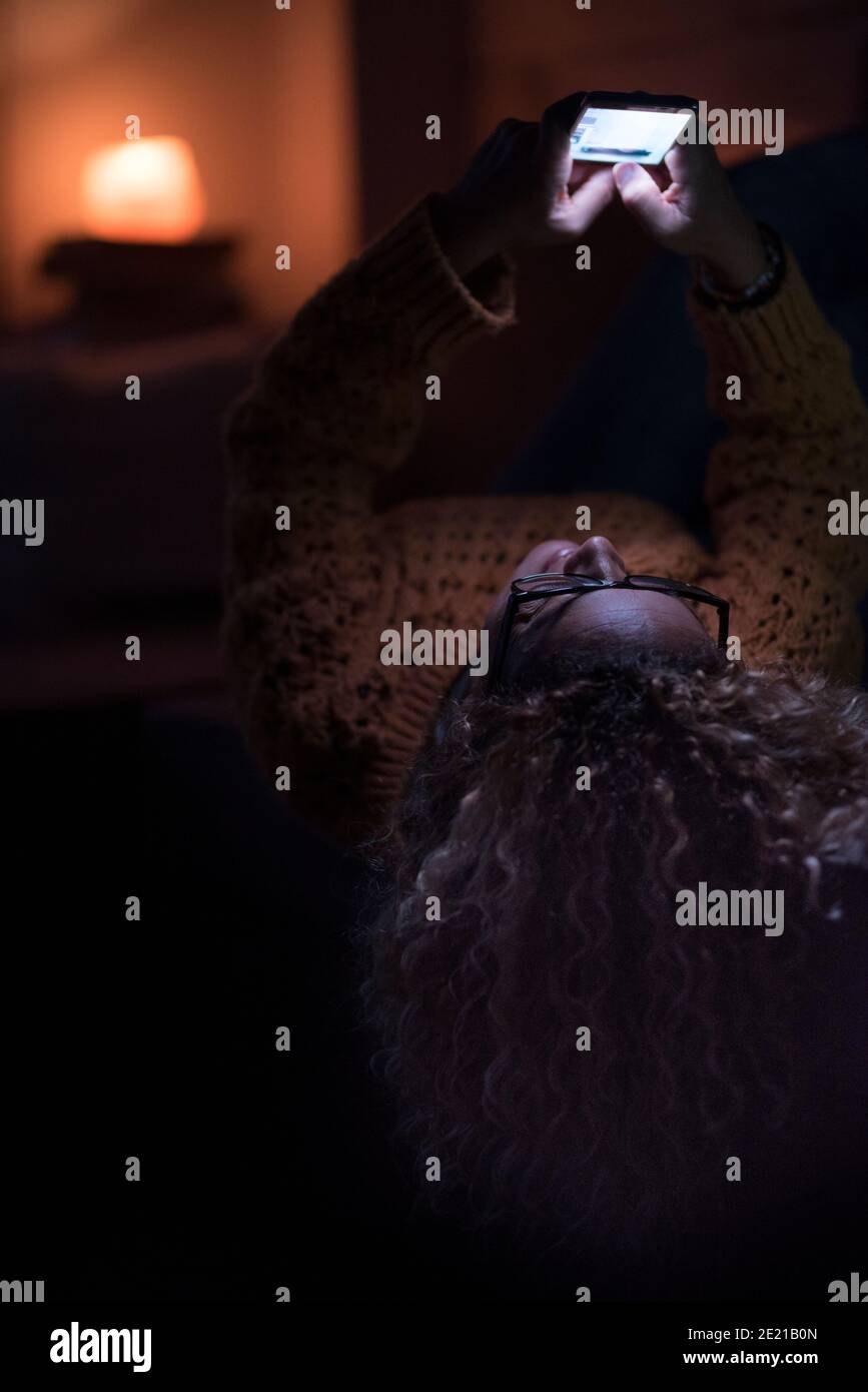 Donna a casa utilizzare il web internet telefono cellulare lahying sul divano di notte - le donne che si stendano sopra il divano godendo il cellulare da solo chattando Foto Stock