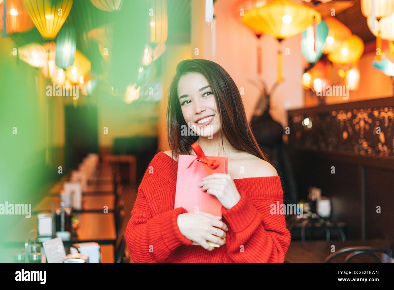 Bella giovane donna asiatica in abiti rossi con regalo rosso Borsa nel ristorante che celebra il Capodanno cinese Foto Stock
