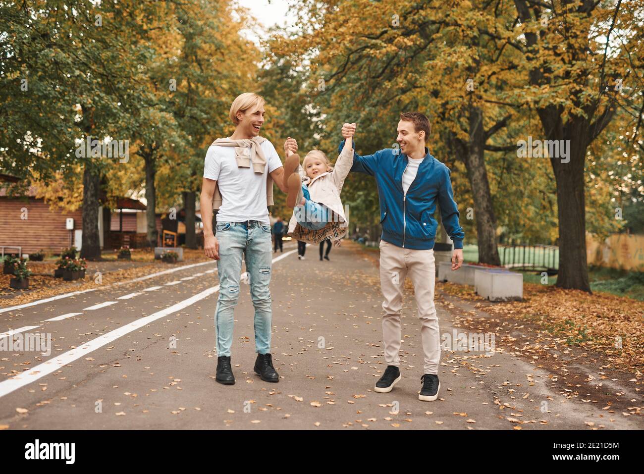 Due genitori gay con la loro figlia adottiva che camminano insieme nel parco. Buon concetto di famiglia LGBT. Foto Stock