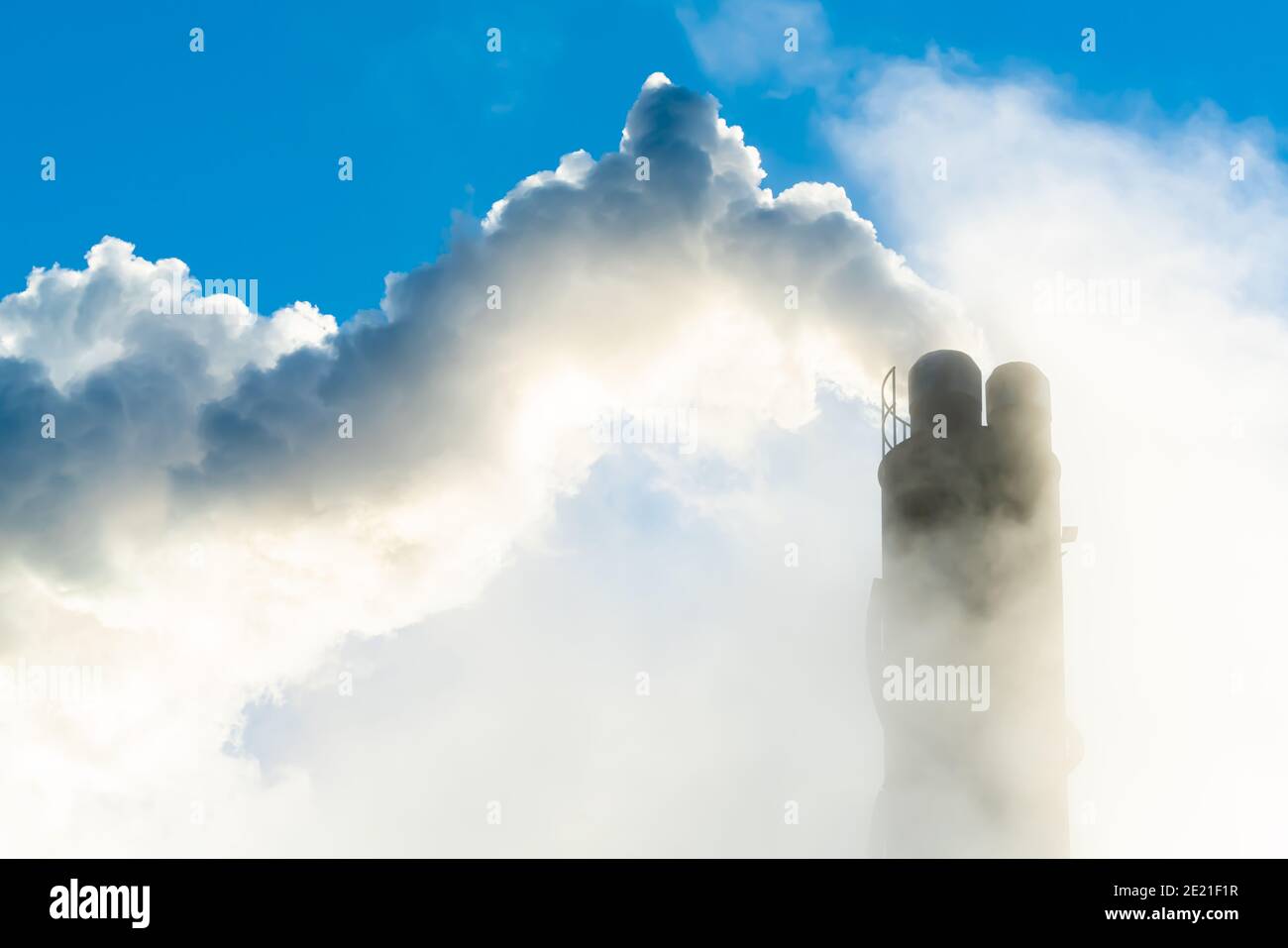 Camino di fumo industriale che mette fuori vapore e fumo su un cielo blu chiaro. Foto Stock