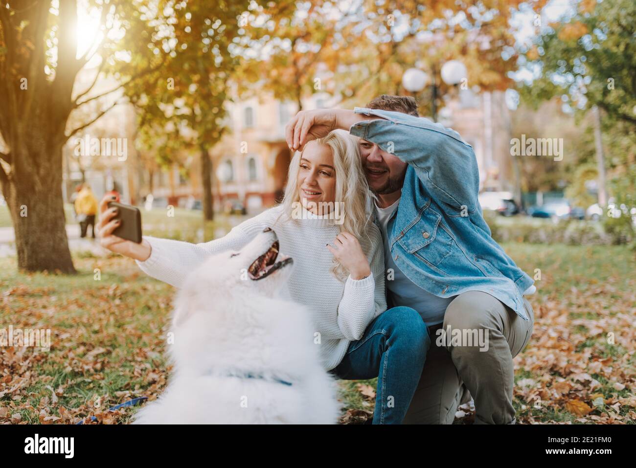 Sorridente bella donna che tiene smartphone mentre fa foto con lei Ragazzo e cane samoyed soffice Foto Stock
