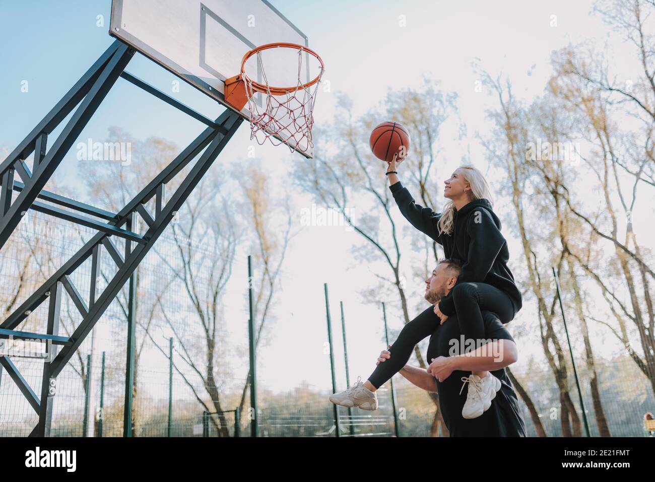 Uomo sorridente e donna che gioca a giocare sul campo di pallacanestro durante giorno di sole Foto Stock