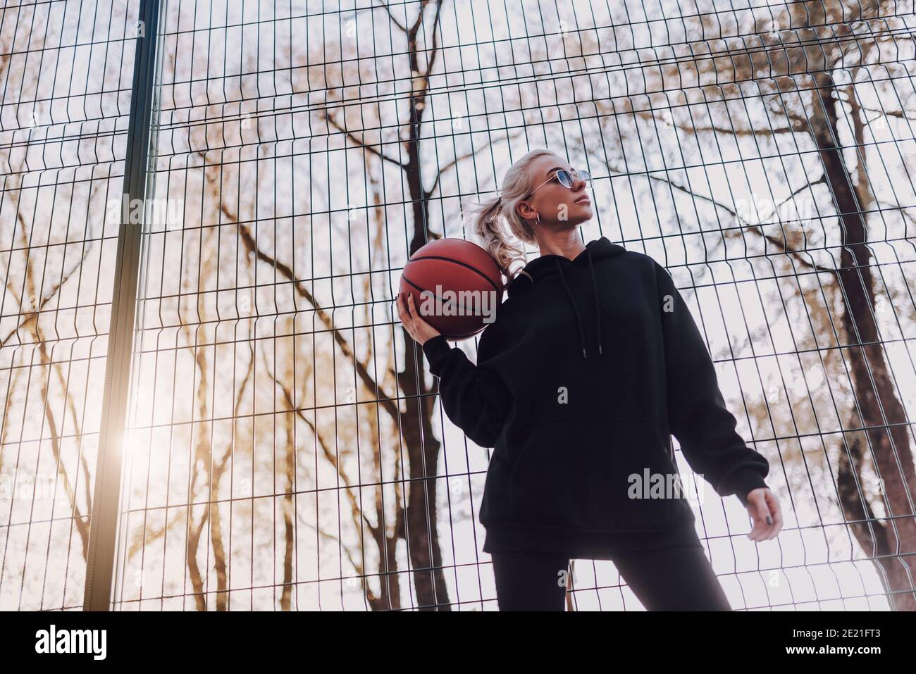 Bella donna atletica in abbigliamento sportivo con palla da basket all'aperto durante giorno di sole Foto Stock