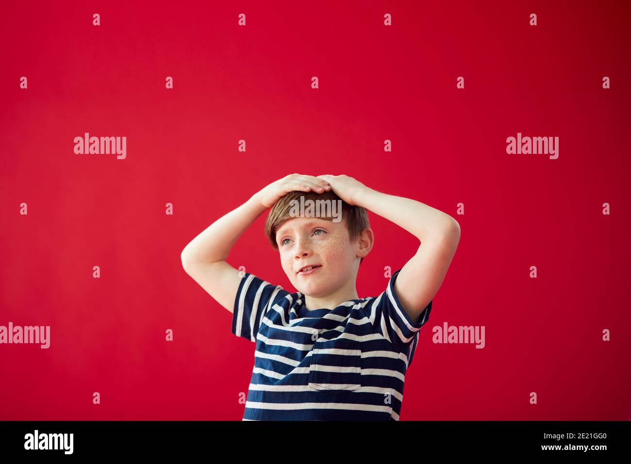 Ritratto di ragazzo sorridente con le mani su testa contro Rosso Studio sfondo Foto Stock