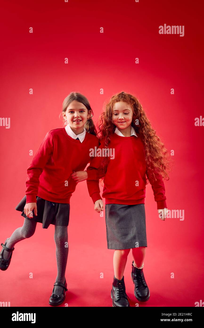 Due allievi della scuola elementare che indossano armi uniformi che collegano contro il rosso Studio sfondo Foto Stock