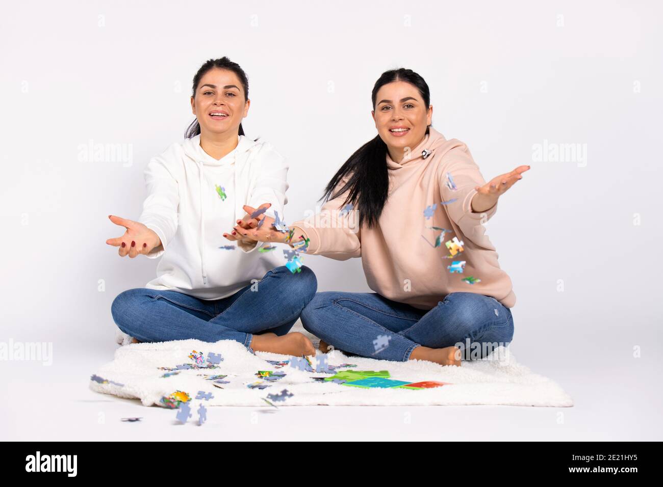 Gemelli sul pavimento, seduti su una morbida coperta, sorridi e lancia il puzzle nella fotocamera. Sfondo bianco. Foto Stock