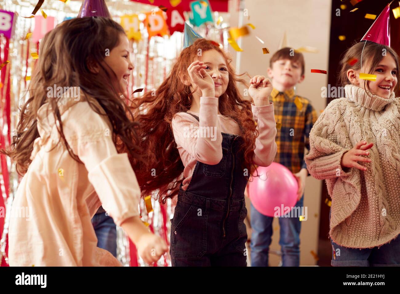 Gruppo di bambini che ballano mentre celebrano al partito di compleanno Con cappelli in carta Foto Stock