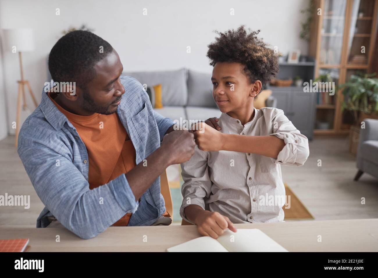 Ritratto del padre afro-americano pugno che urla sorridendo figlio mentre fa compiti insieme a casa Foto Stock
