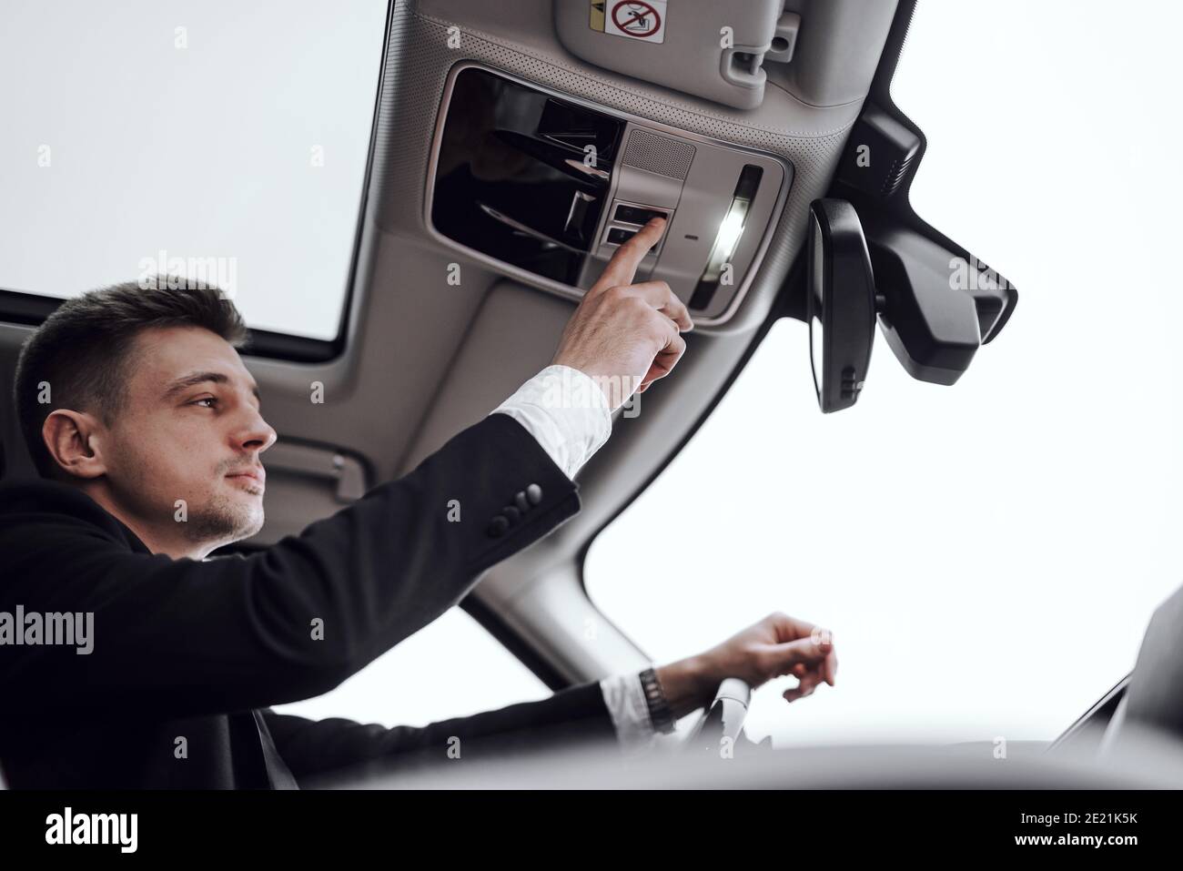 Giovane uomo d'affari sicuro seduto in auto mentre si accende la luce. Affitto e concetto di permuta Foto Stock