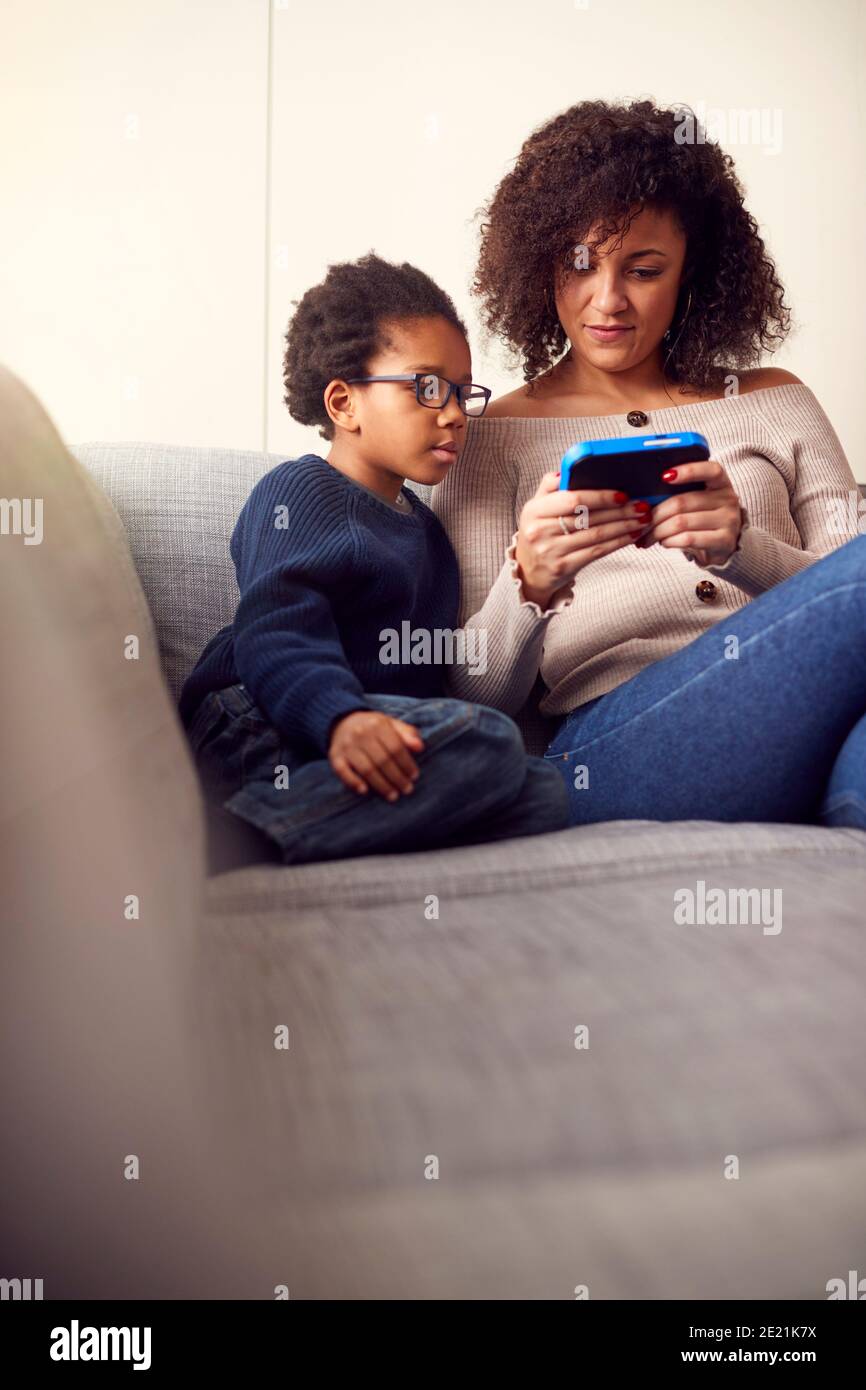Madre e figlio seduti sul divano a casa giocando computer Gioca insieme su un dispositivo portatile a casa Foto Stock