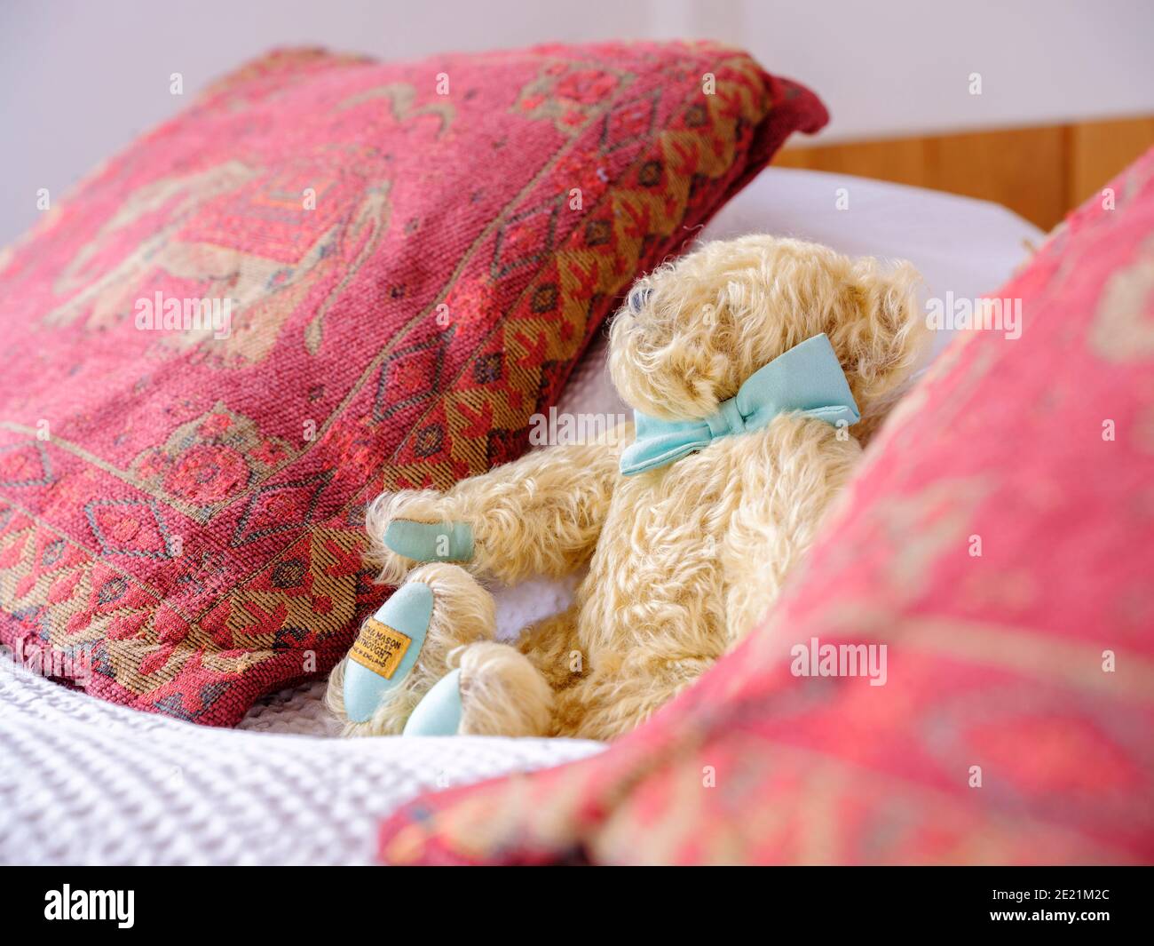 Un orsacchiotto su un letto fatto con cuscini rossi su entrambi i lati. Foto Stock