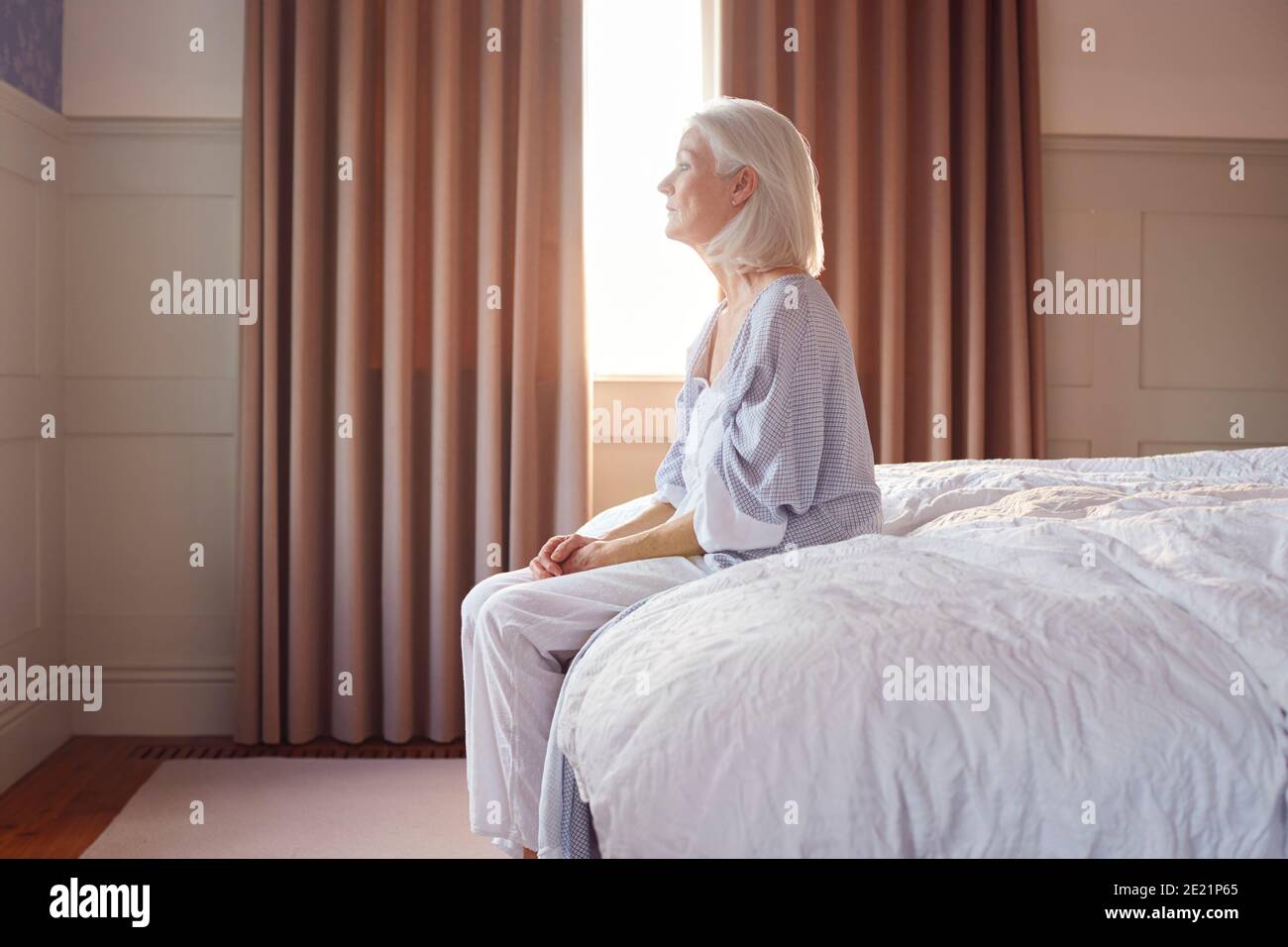 Donna anziano infelice e depressa seduta sul bordo del letto A casa Foto Stock