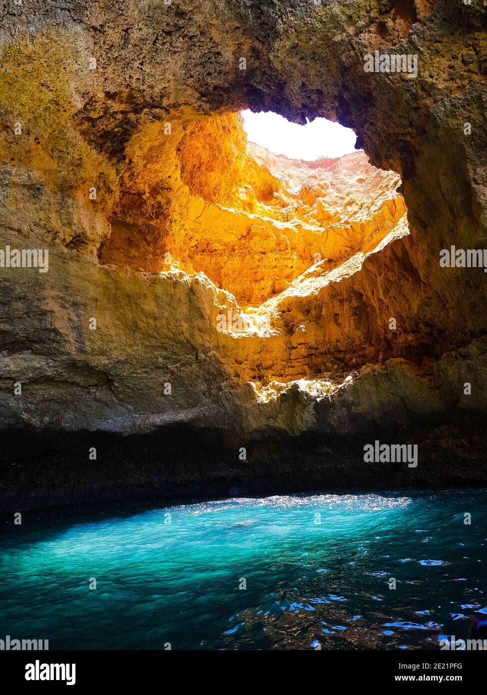 Il sole passa attraverso un buco della Grotta di Benagil, in Portogallo, dando uno spettacolare colore blu all'acqua di mare. Foto Stock