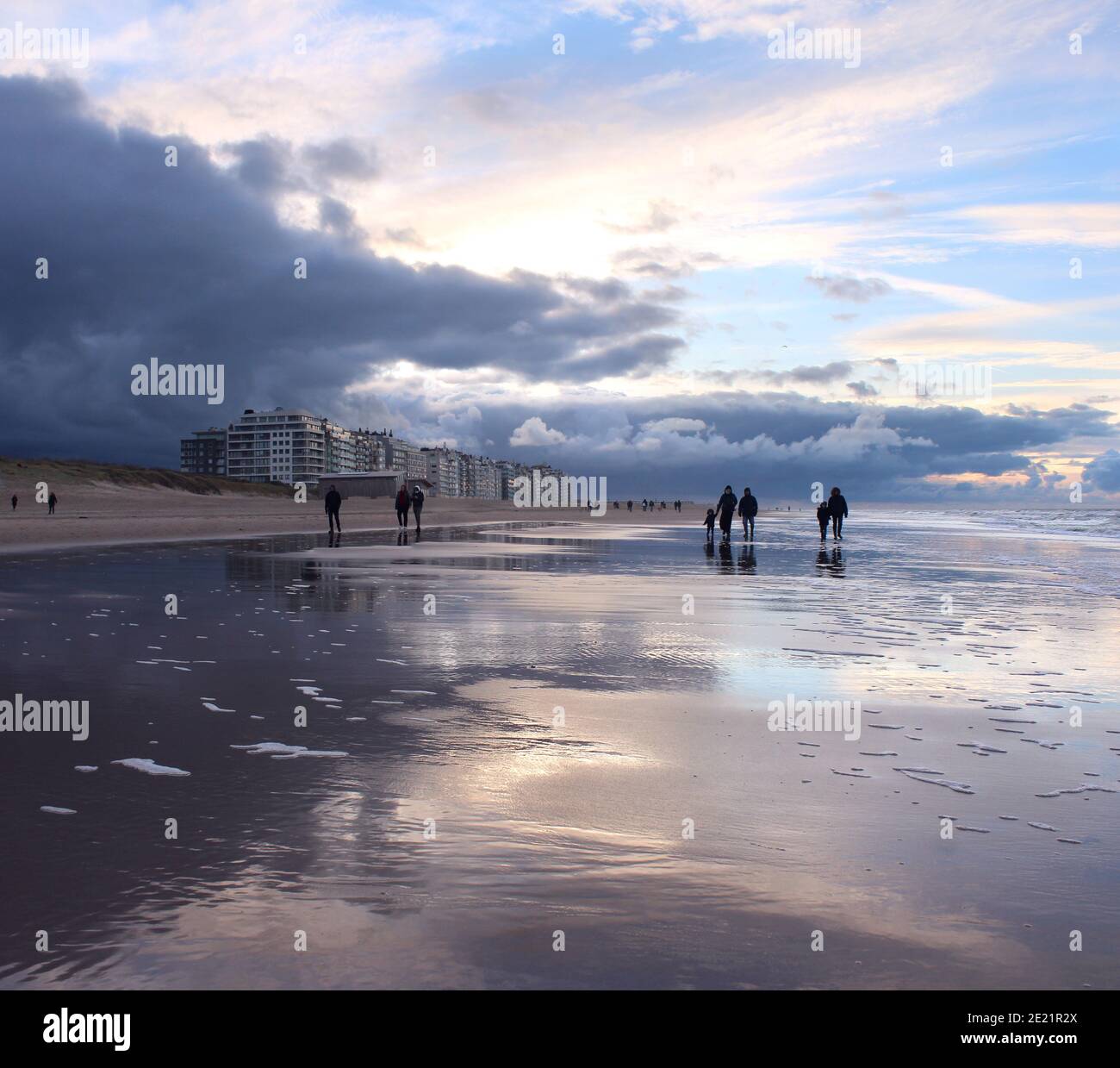 La gente fuori cammina sulla spiaggia durante un tramonto d'inverno a Wenduine, Fiandre Occidentali, Belgio Foto Stock