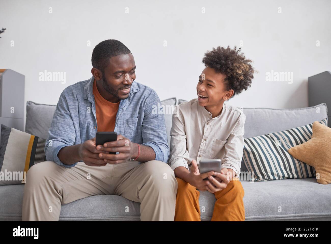 Adolescente gioioso divertirsi con suo padre giocando a videogiochi su smartphone insieme mentre si è a casa, medio lungo scatto Foto Stock