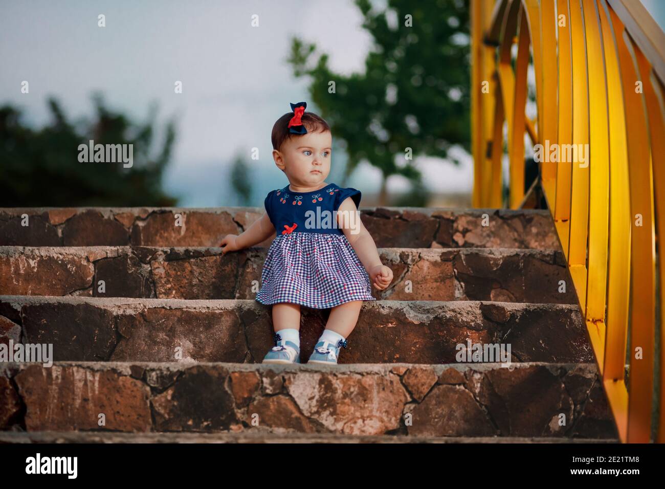 Scatto serale di nove mesi adorabile bambino seduto sulle scale e guardando il reticolo di giardino Foto Stock