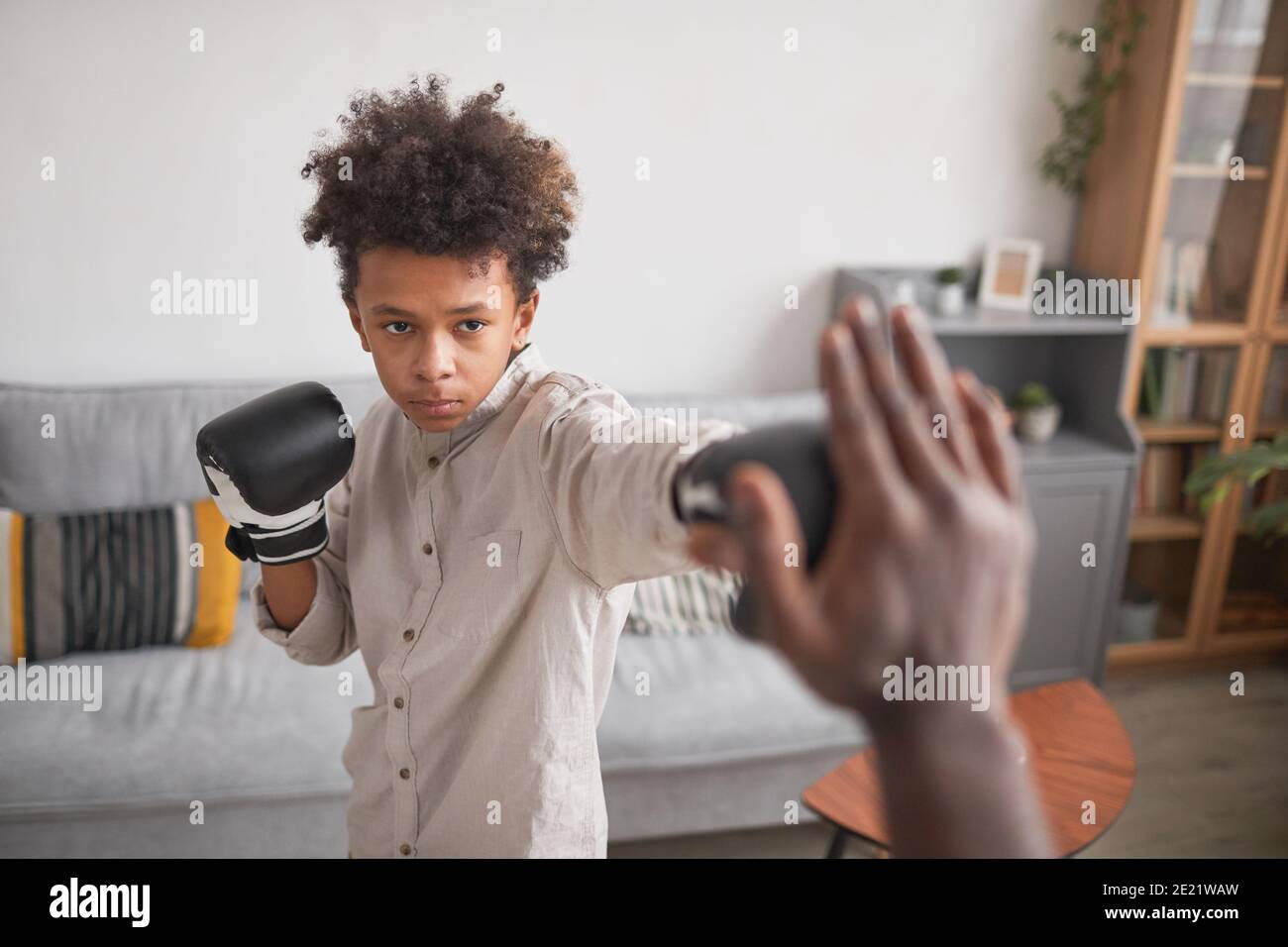 Ritratto medio di un serio ragazzo afro-americano che indossa la boxe guanti di addestramento pugni con suo padre a casa Foto Stock
