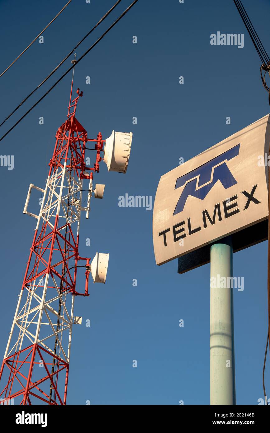 Una torre cellulare rossa e bianca e un grande segno per Compagnia cellulare in Messico sostenuta da un cielo blu chiaro Foto Stock