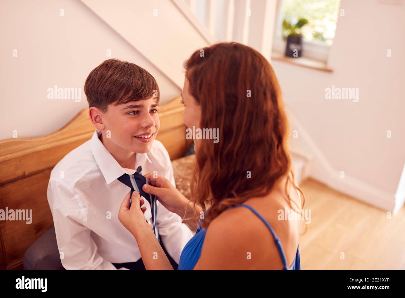 Madre che aiuta Son a legare Necktie prima che lasci la sede Per il primo giorno a High School Foto Stock
