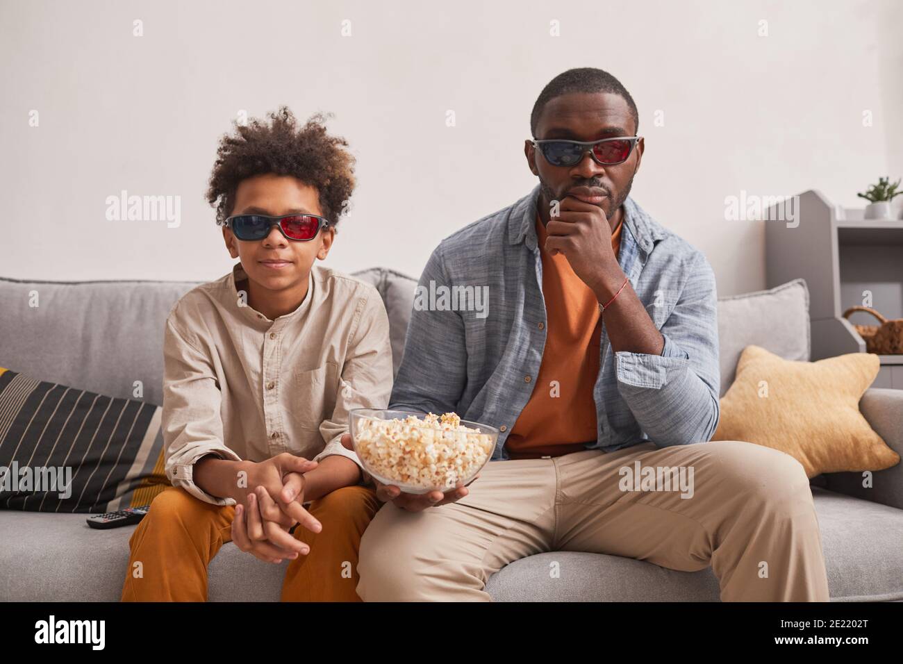 Moderno uomo di famiglia afroamericano e suo figlio teen seduto Sul divano nel soggiorno, guardare film in 3D e mangiare popcorn Foto Stock