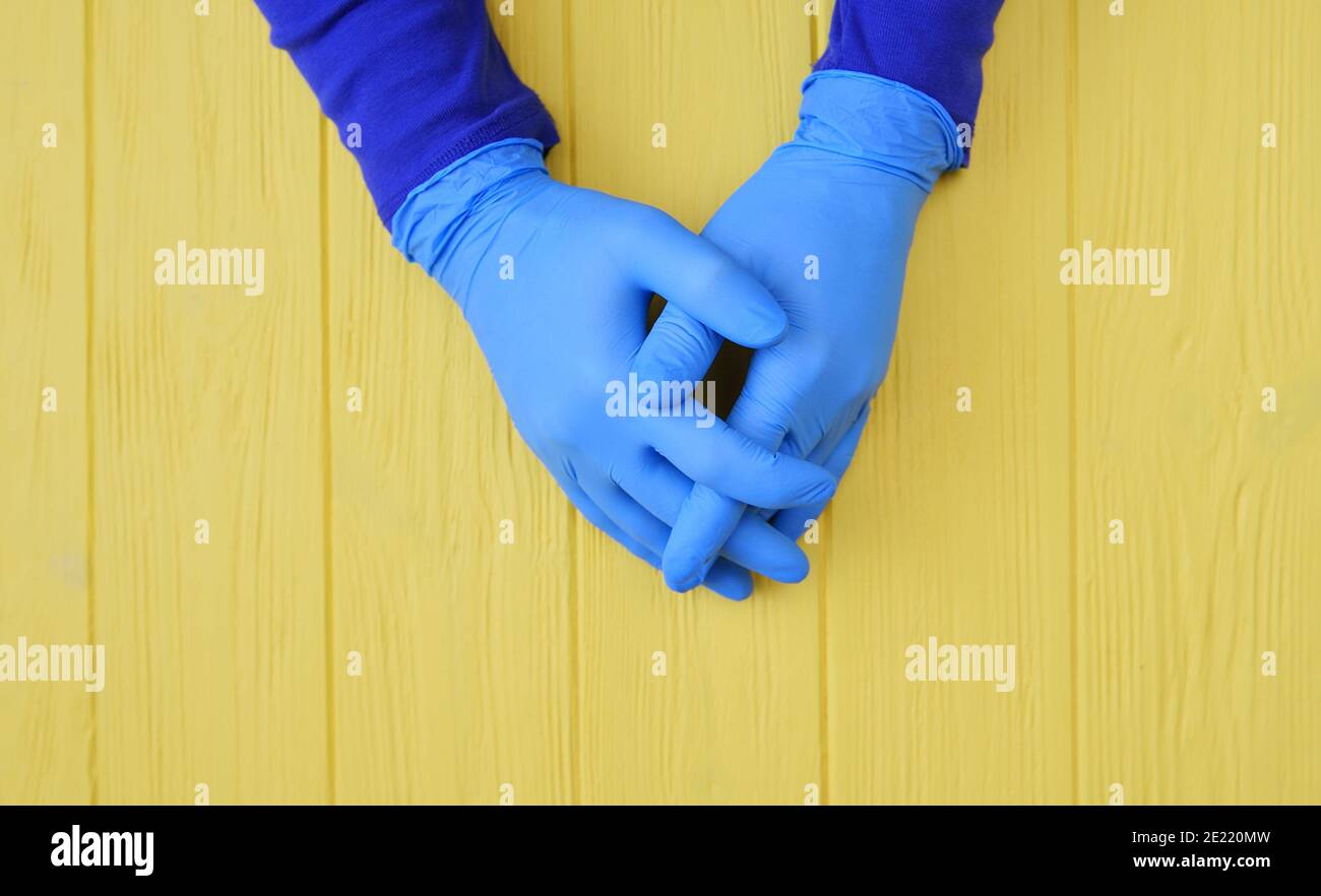 Le mani blu con guanti si avvicinano su sfondo giallo di legno. Richiedere la disinfezione delle mani. Arrestare il concetto di coronavirus. Uso di gel antibatterico per le mani durante Foto Stock