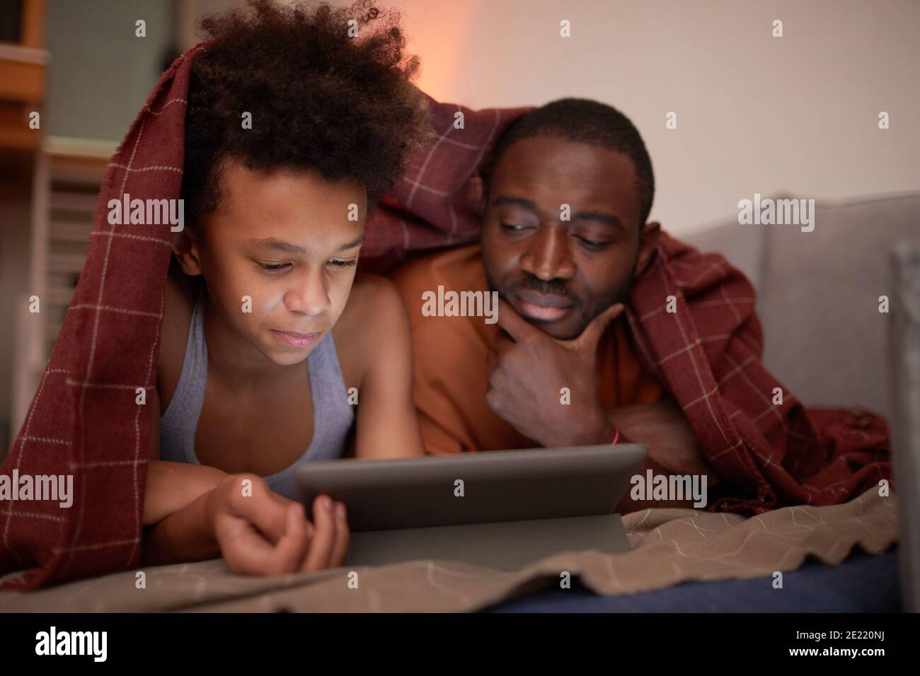 Il padre moderno trascorre la serata con il suo bel figlio a casa guardare i cartoni animati online su un tablet digitale Foto Stock