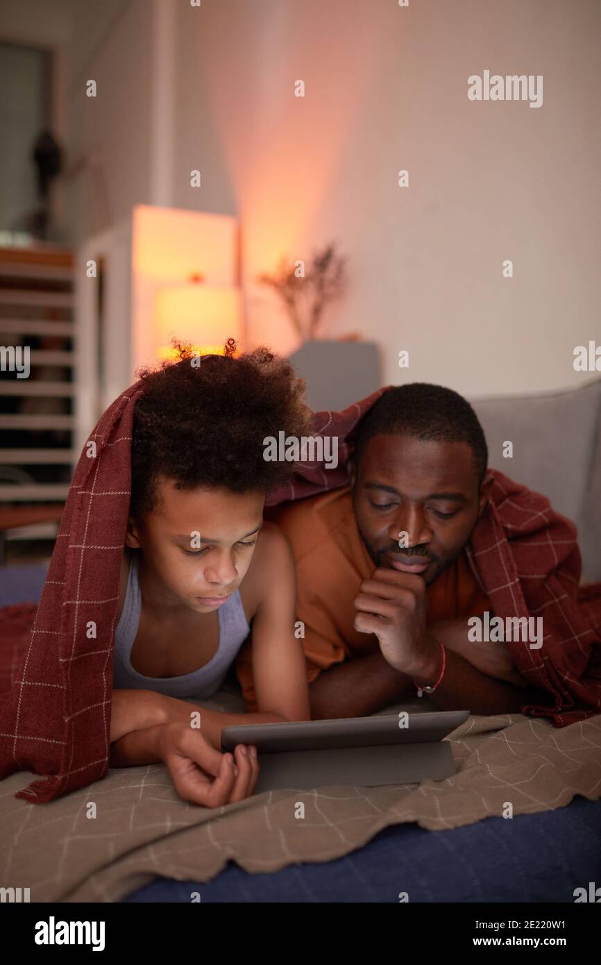 Il padre amorevole che passa la sera accogliente con il suo figlio teen a. home relax sotto coperta guardare film on-line su tablet digitale Foto Stock