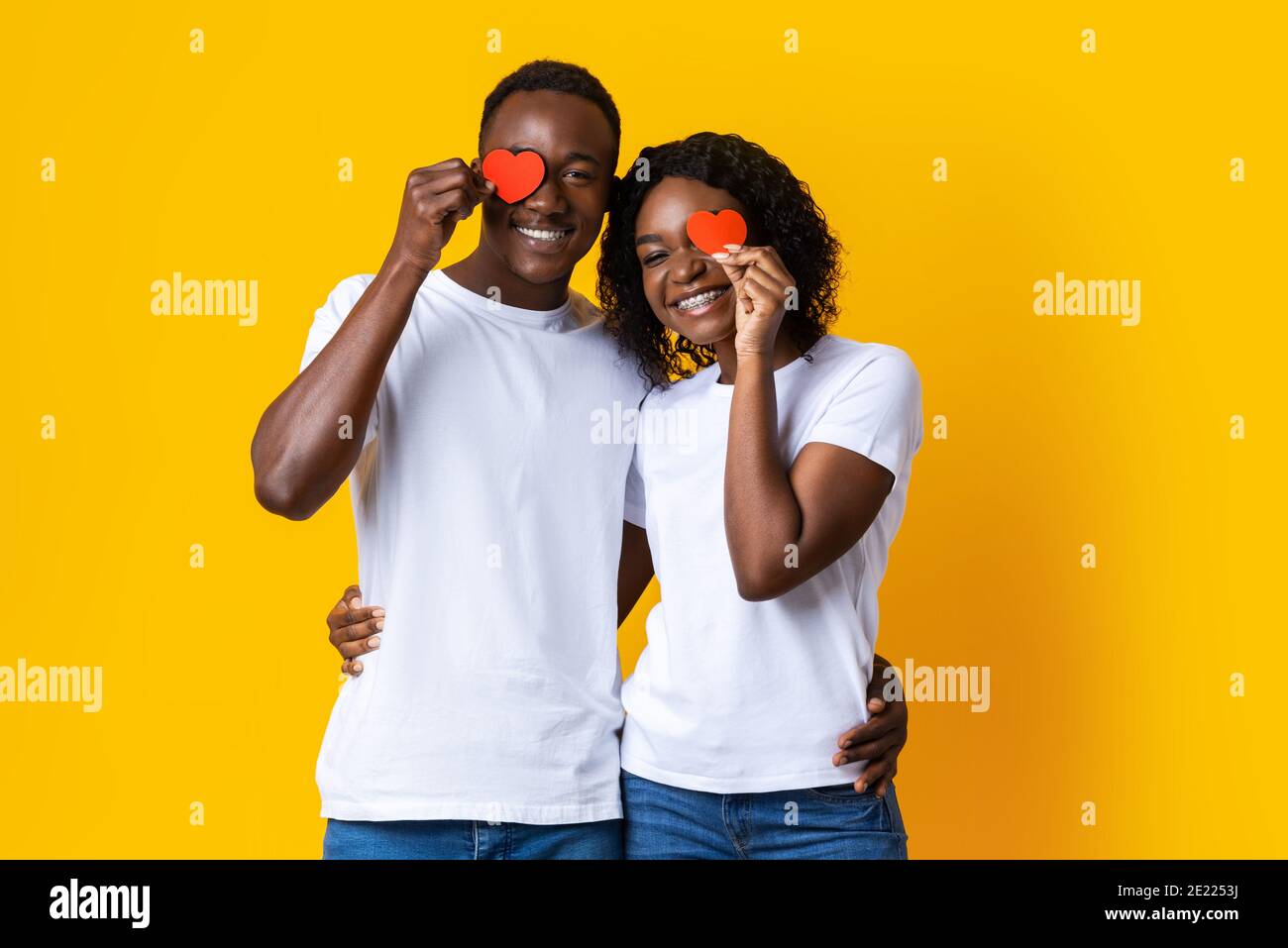 Gli amanti neri abbracciano e tengono i cuori rossi sul giallo Foto Stock