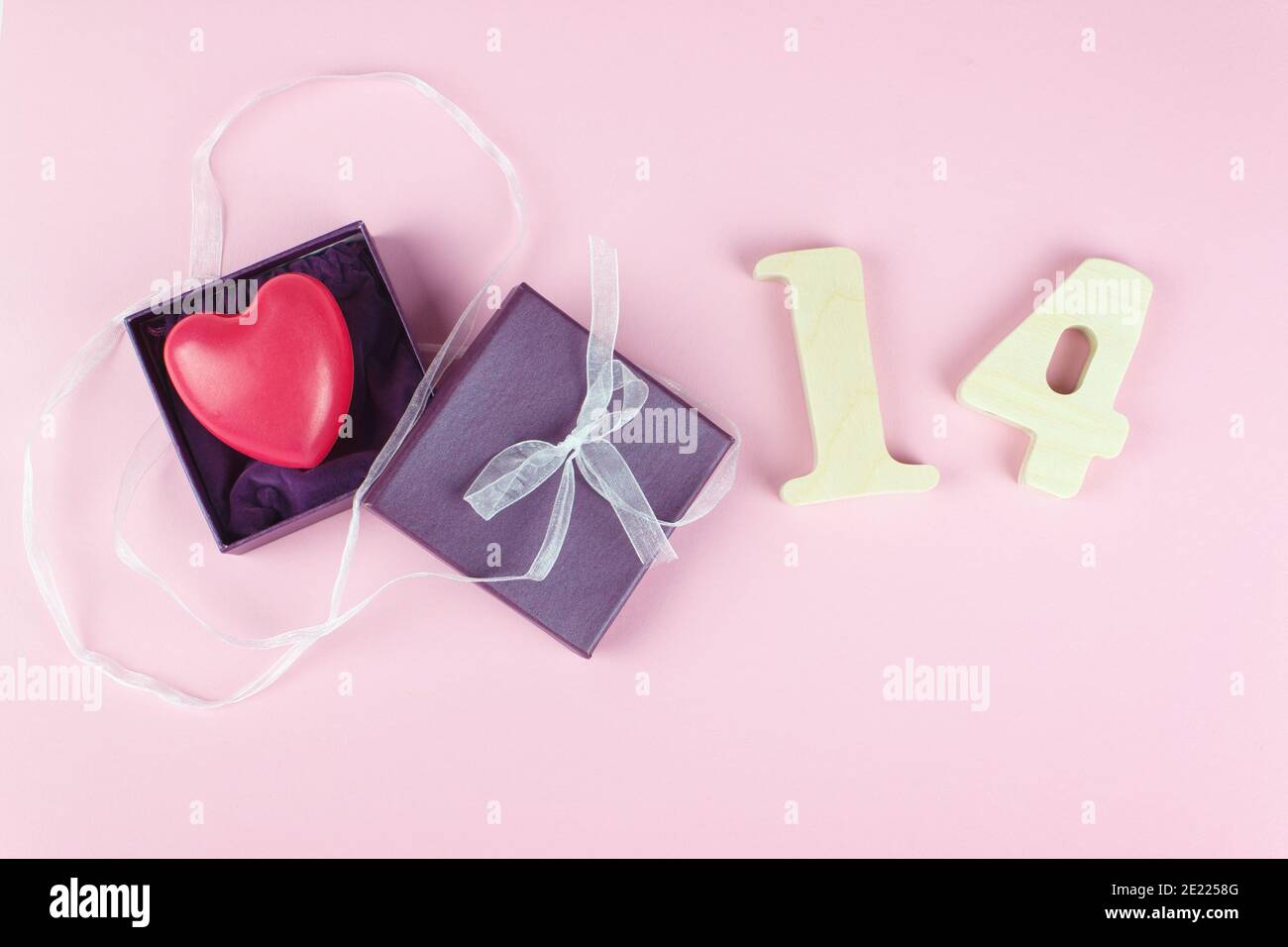 Confezione regalo di colore viola con cuore rosso e il numero 14 di legno su sfondo rosa. Concetto di San Valentino Foto Stock