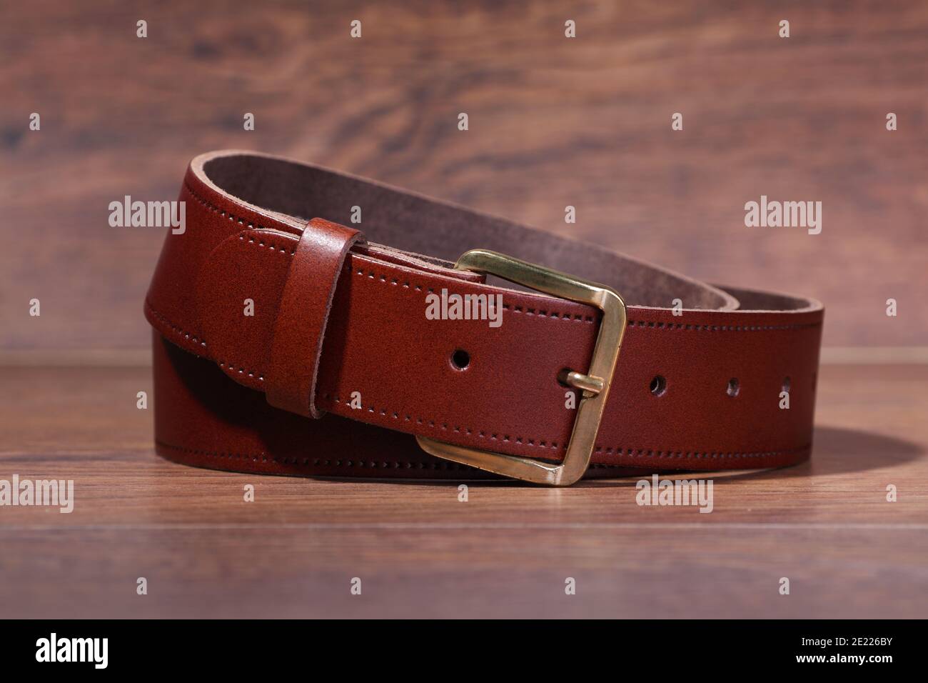 cintura marrone di cuoio arrotolata su uno sfondo di legno Foto Stock