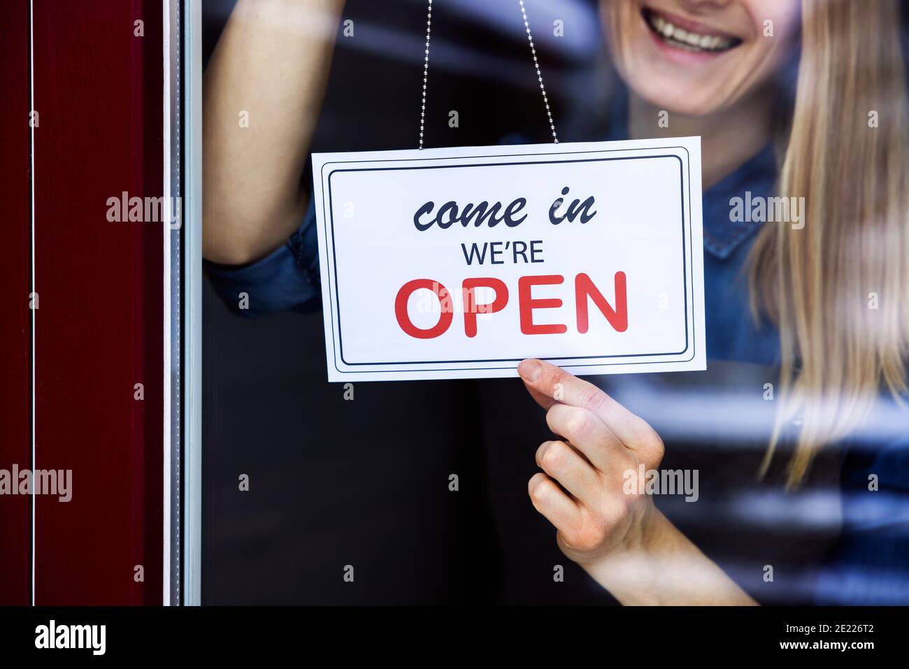 donna sorridente appesa all'insegna aperta sul piccolo negozio di affari locale finestrino della portiera Foto Stock