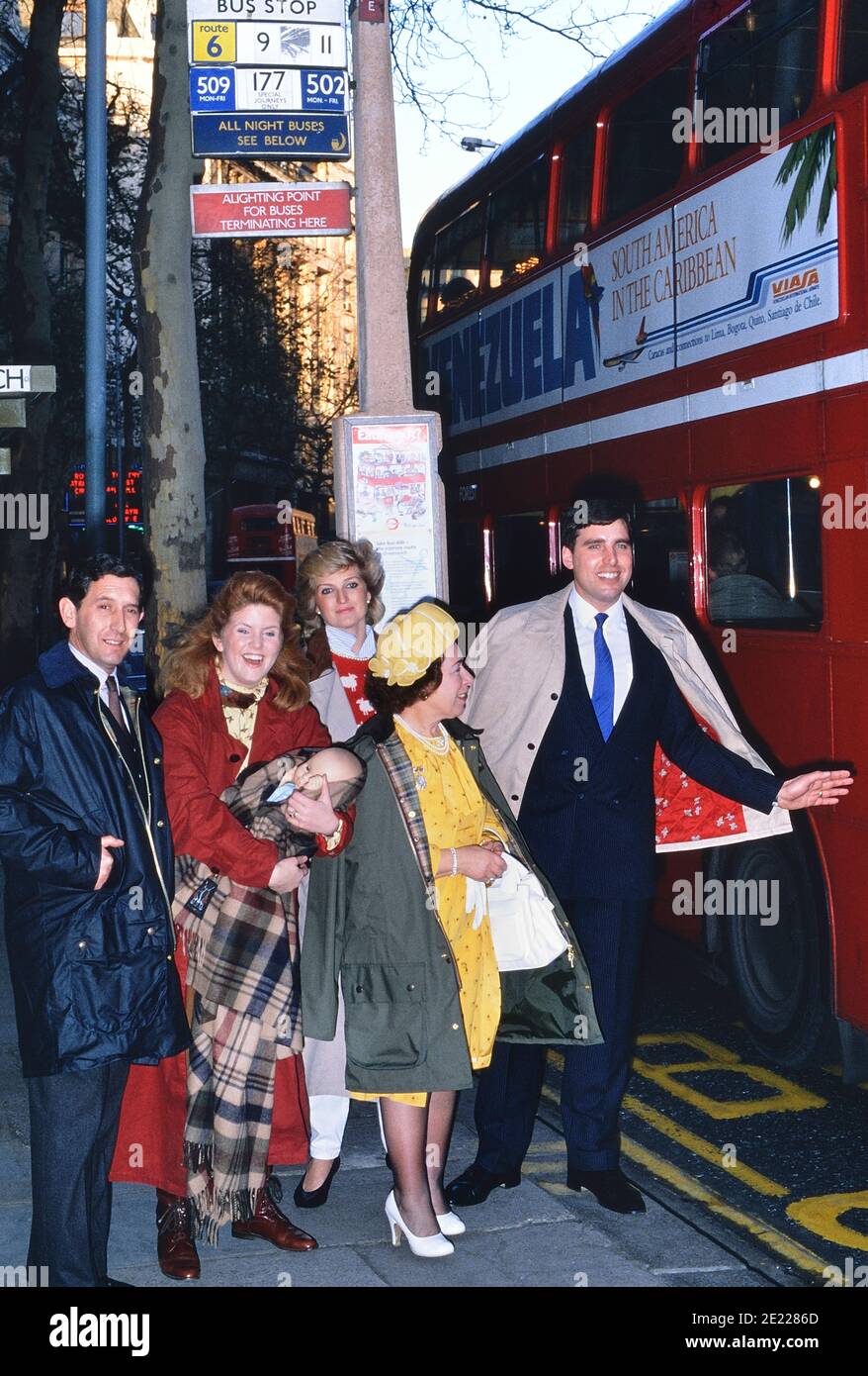 Un gruppo di impersonatori della famiglia reale Britannica che accodano ad una fermata dell'autobus per prendere un autobus rosso a due piani. Londra. Inghilterra, Regno Unito, circa 1989 Foto Stock