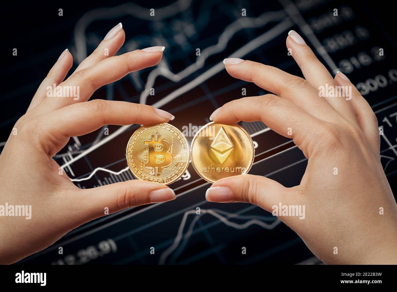 mani femmina macro che tengono il bitcoin e l'etereo fianco a fianco di fronte al grafico del mercato azionario Foto Stock