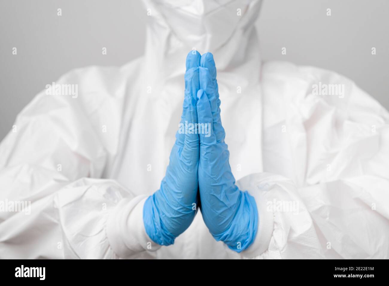 Dottore in una tuta protettiva contro il rischio biologico e maschera protettiva contro il coronavirus, Sars-Cov-2, Covid-19 che prega in guanti di gomma blu. Foto Stock