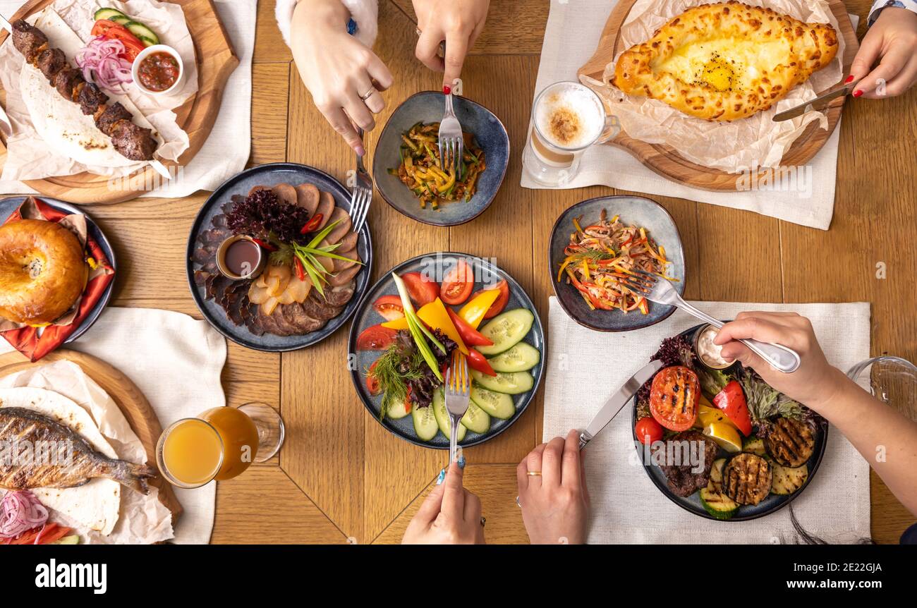 Tavolo da pranzo con vari piatti vista dall'alto, gruppo di persone che cenano insieme. La gente usa le posate. Foto Stock