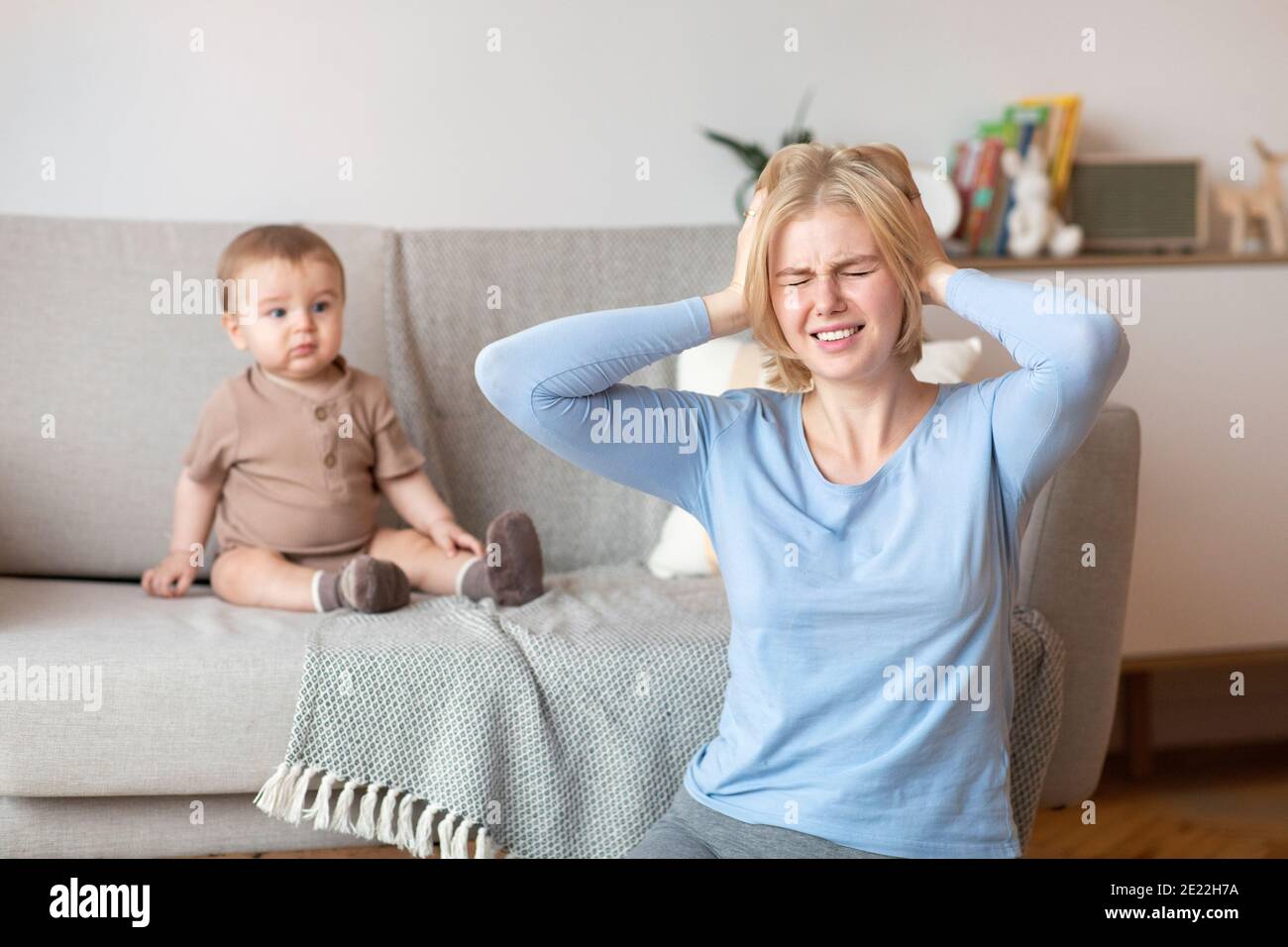 Madre stressata che soffre di mal di testa, seduta con il bambino a casa Foto Stock