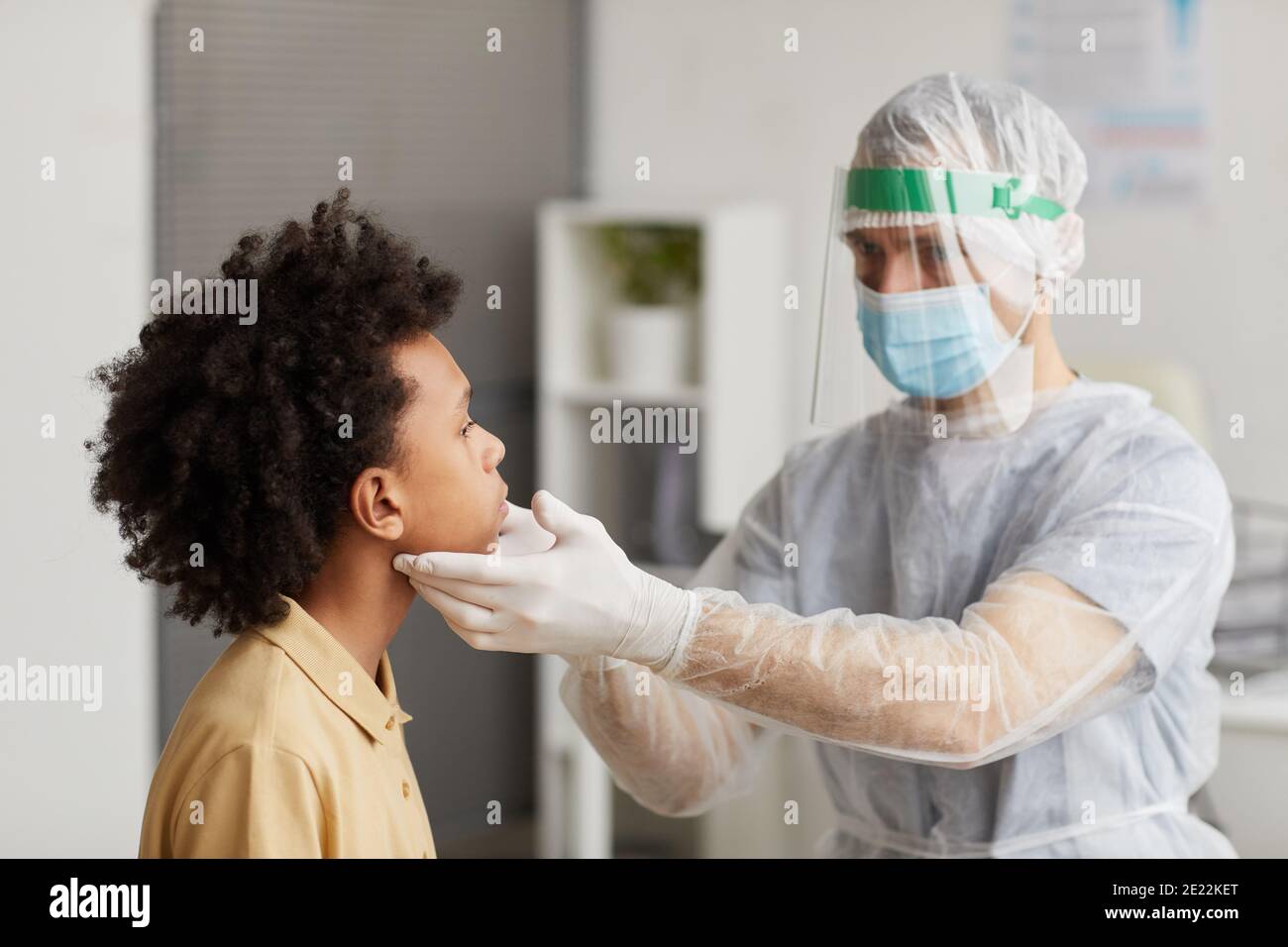 Ritratto di medico che indossa attrezzatura protettiva completa che esamina il ragazzo durante la consultazione in clinica, copia spazio Foto Stock