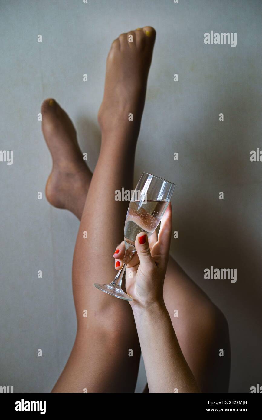 Crop anonimo femmina in nylon collant con gambe rialzate e. bicchiere di bevanda alcolica alla luce del giorno Foto Stock
