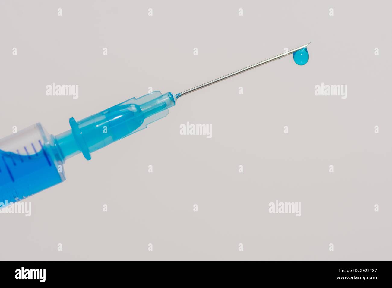 siringa con un vaccino fluido blu e una goccia su lo sfondo frontale obliquo e bianco Foto Stock