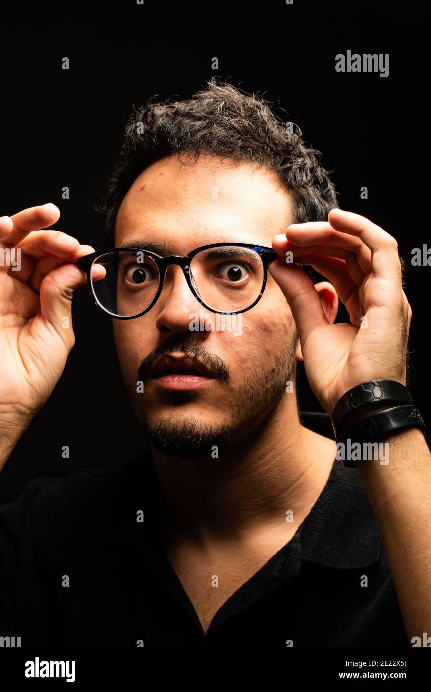 L'uomo con gli occhiali fissa la macchina fotografica vestita con una polo nera mentre tiene i suoi occhiali lontano dal viso. Sfondo nero. Concetto ottico Foto Stock