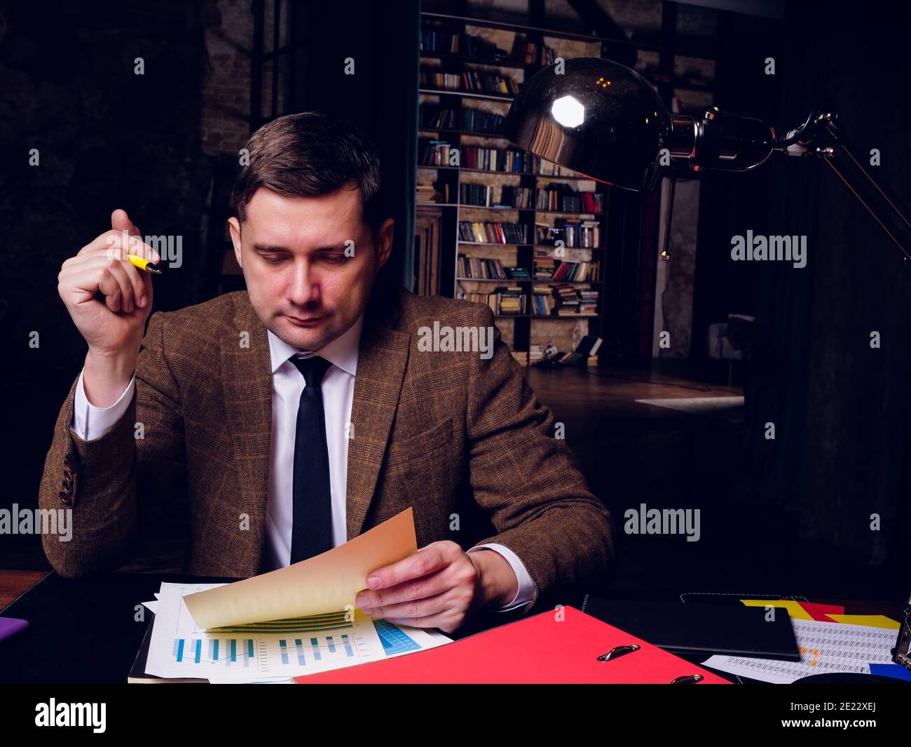 Un uomo in tuta lavora a tarda notte con documenti di lavoro nel suo ufficio. Foto Stock