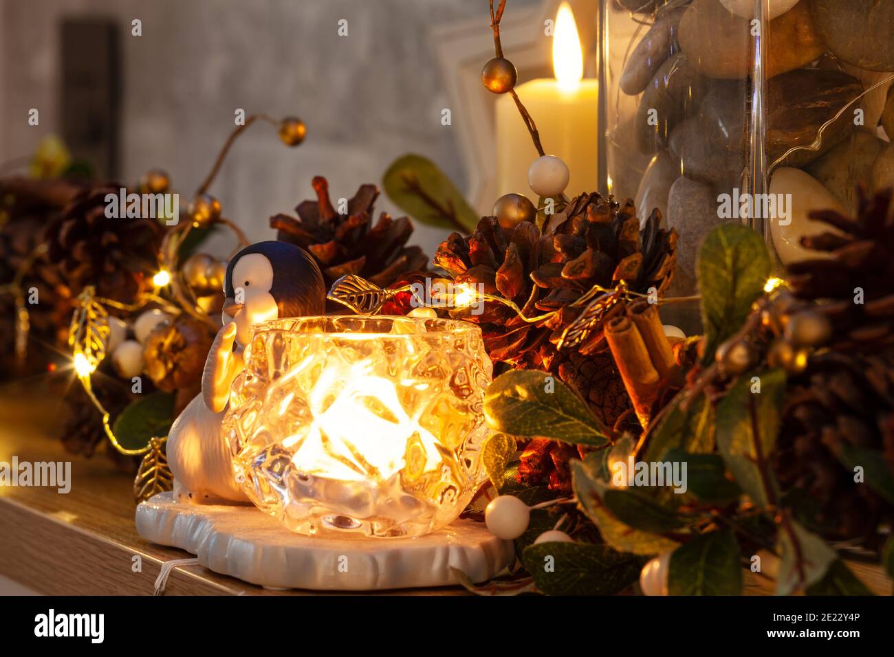 Penguin accanto a una candela su un pezzo di mannola con Natale pinecone ghirlanda e foglia d'oro fata luci Foto Stock