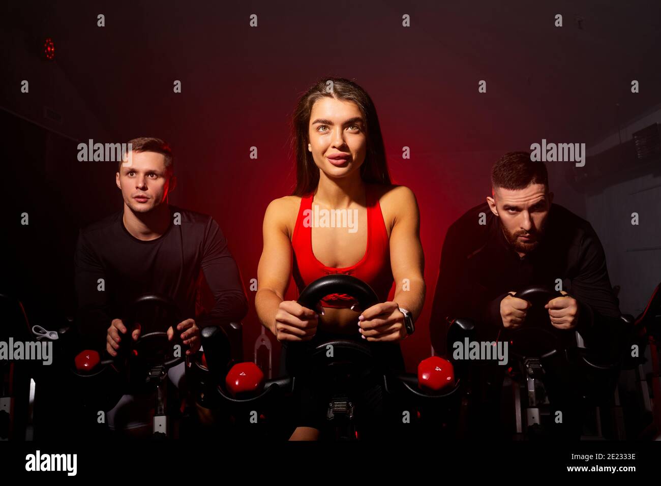 persone attive che si allenano a attrezzature sportive in palestra, fiduciosamente guardando avanti, indossando tute sportive in ambienti bui fumosi Foto Stock