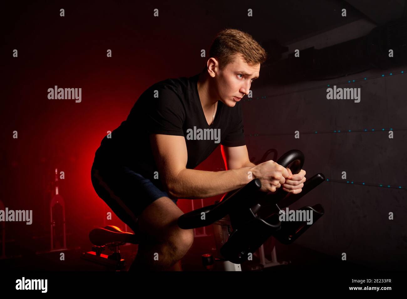 l'allenamento dell'uomo in palestra con attrezzature sportive, un uomo forte e sicuro in tuta ha un allenamento intensivo in bicicletta nel fitness club Foto Stock